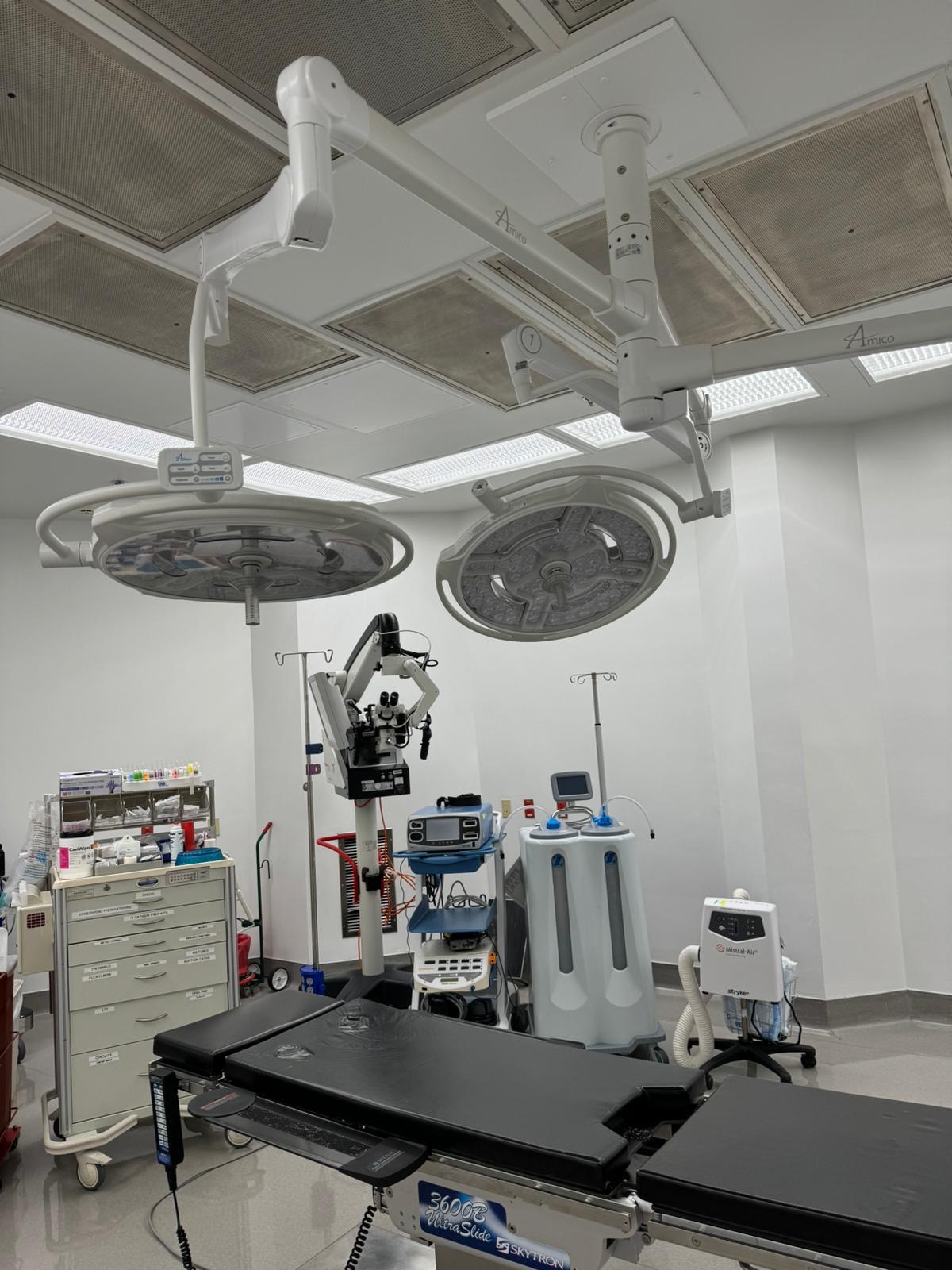 Wider view of the Amico ceiling-mounted surgical lights and suspension arms above an operating table.