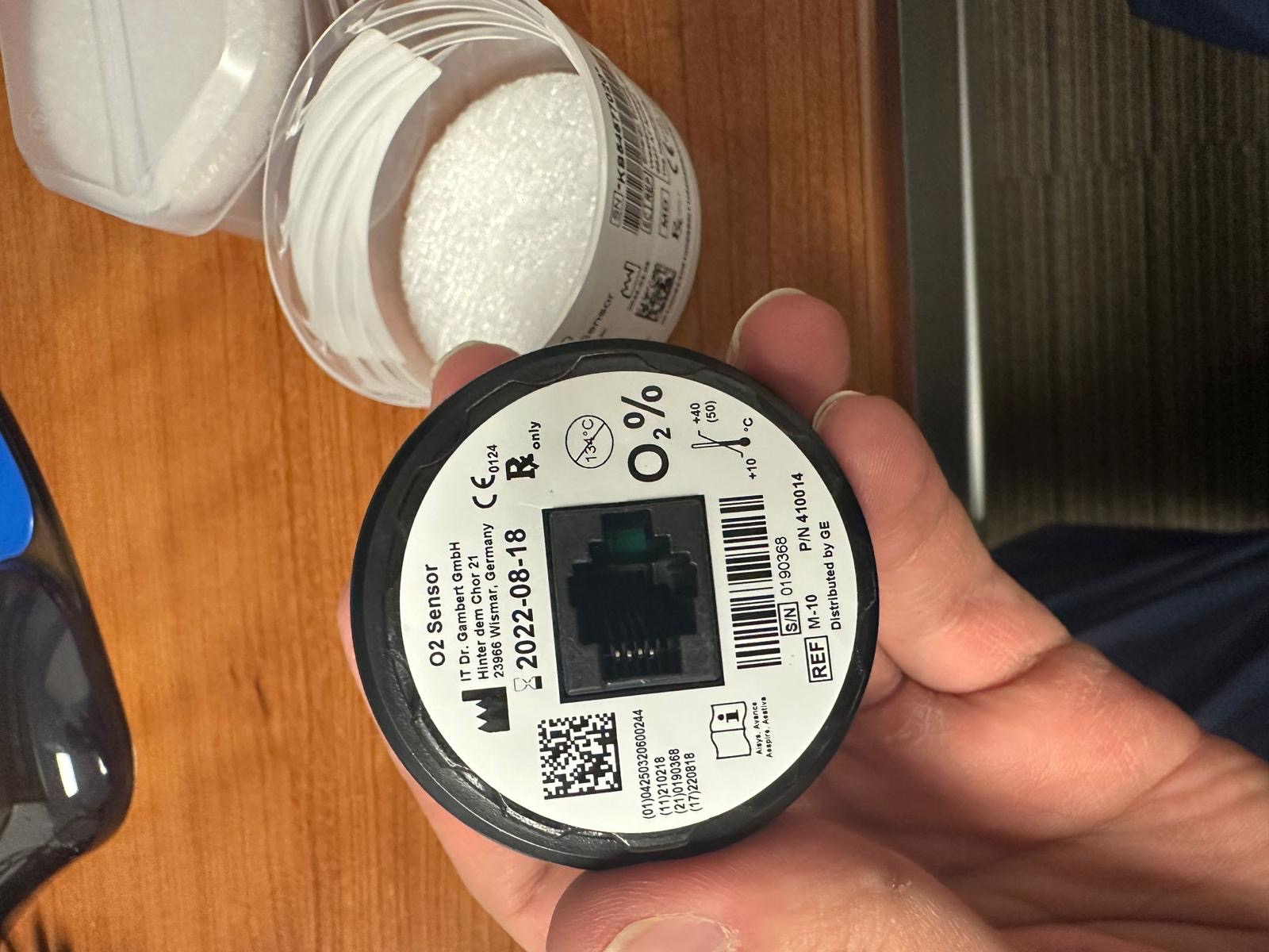 Anesthesia oxygen sensor with O2 label and electrical connector held during sensor replacement.