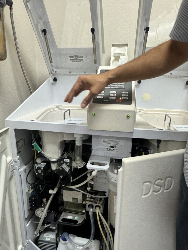 Biomedical service work on an endoscope reprocessor with the front panel open and internal components visible
