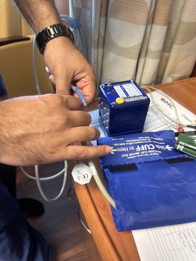 Hands connecting a blood pressure cuff to a test simulator during biomedical equipment maintenance