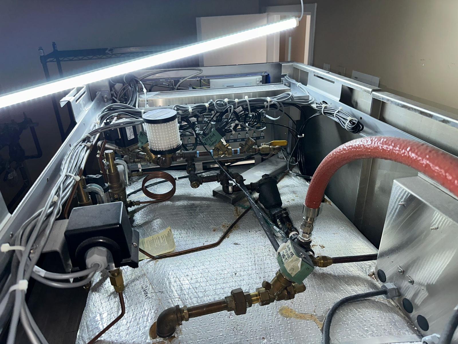 Getinge sterilizer piping and valve assemblies above the insulated chamber during corrective service.