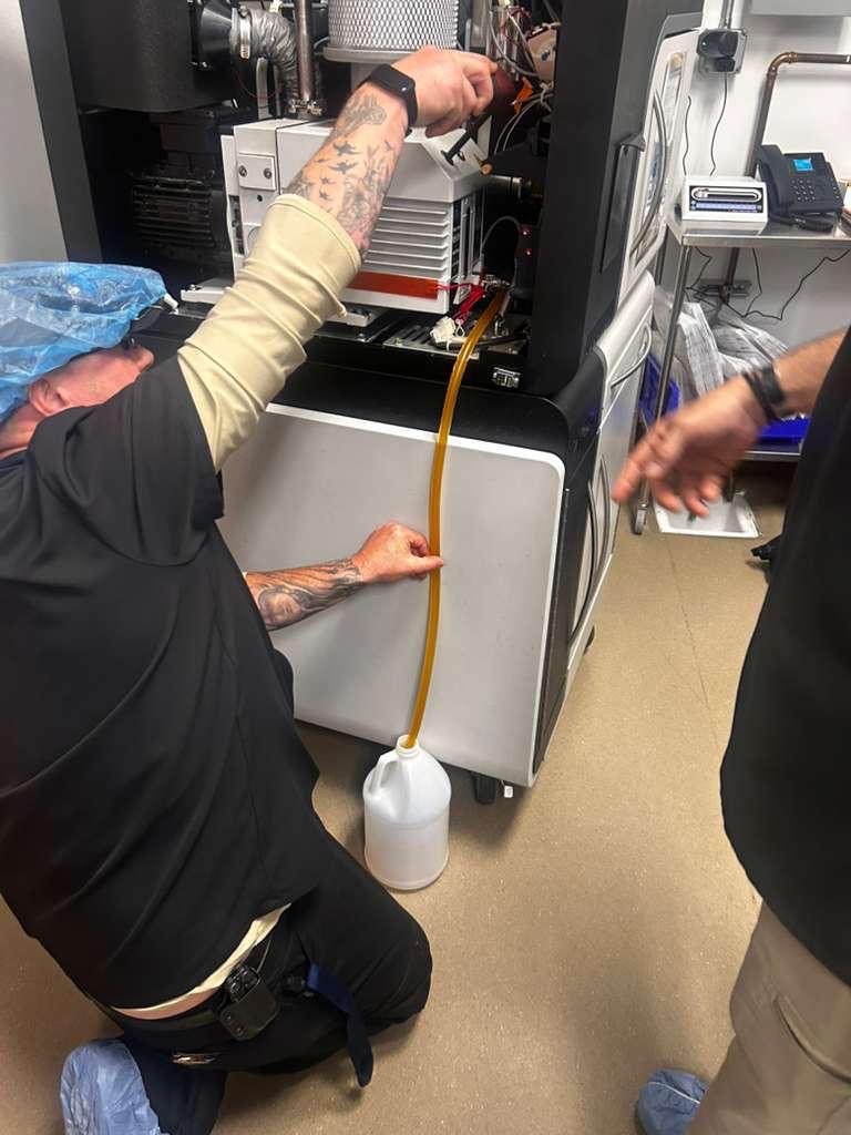 Vacuum pump oil draining through a hose into a collection container during STERIS V-PRO 60 service.