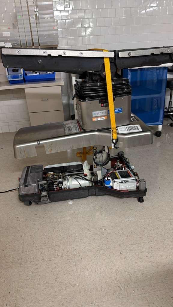 STERIS surgical table with base covers removed and battery compartment accessible during replacement.